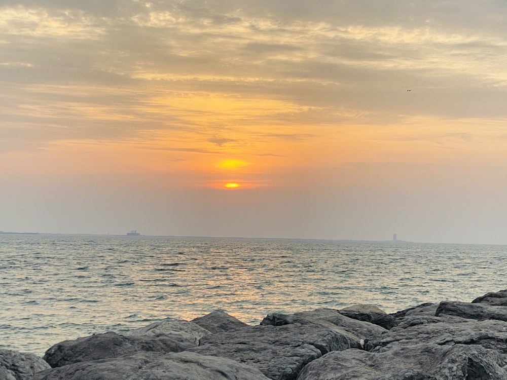 rochas cinzentas perto do corpo de água durante o pôr do sol
