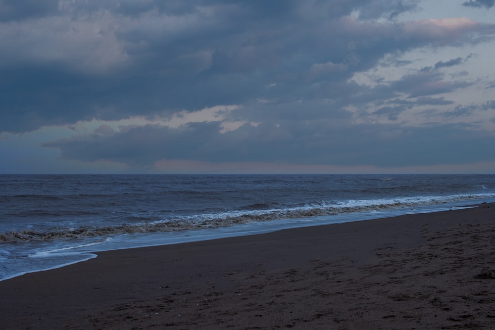 ocean waves crashing on shore under cloudy sky during daytime