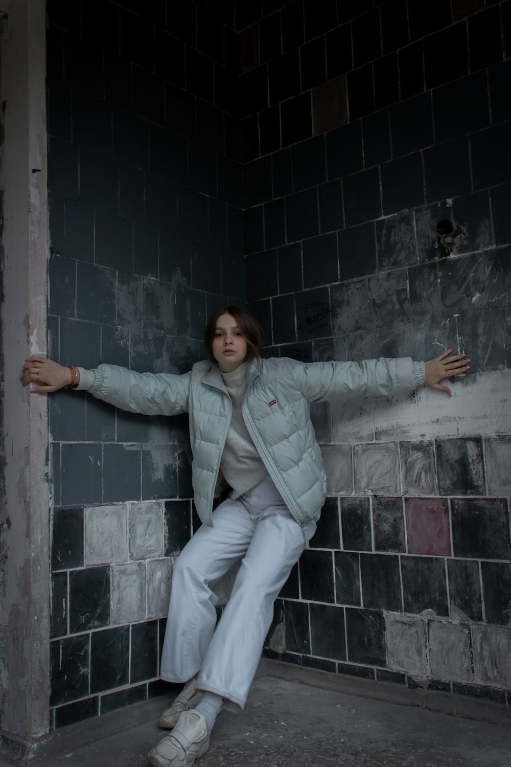 woman in gray jacket and white pants sitting on gray concrete wall