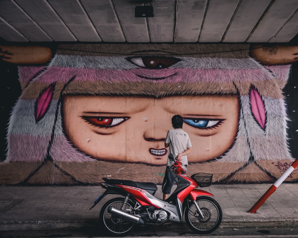 red and black motorcycle parked beside wall with graffiti