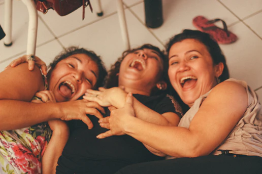 Trois femmes souriantes se tiennent près d'un mur blanc