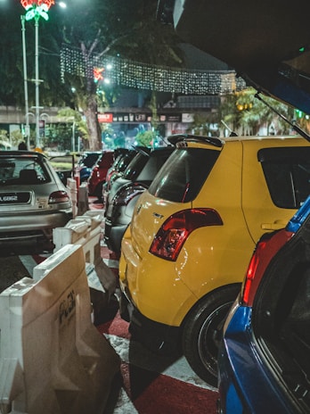 Bright, well-lit parking lot with orderly parked cars near a busy urban street.