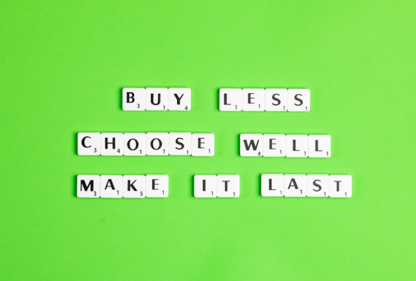White letter tiles arranged on a bright green background spell out the message 'BUY LESS, CHOOSE WELL, MAKE IT LAST'.