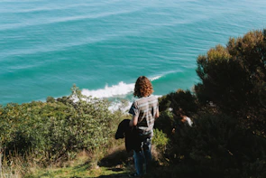 A woman standing on a cliff overlooking a vast turquoise ocean, her hair catching the breeze.