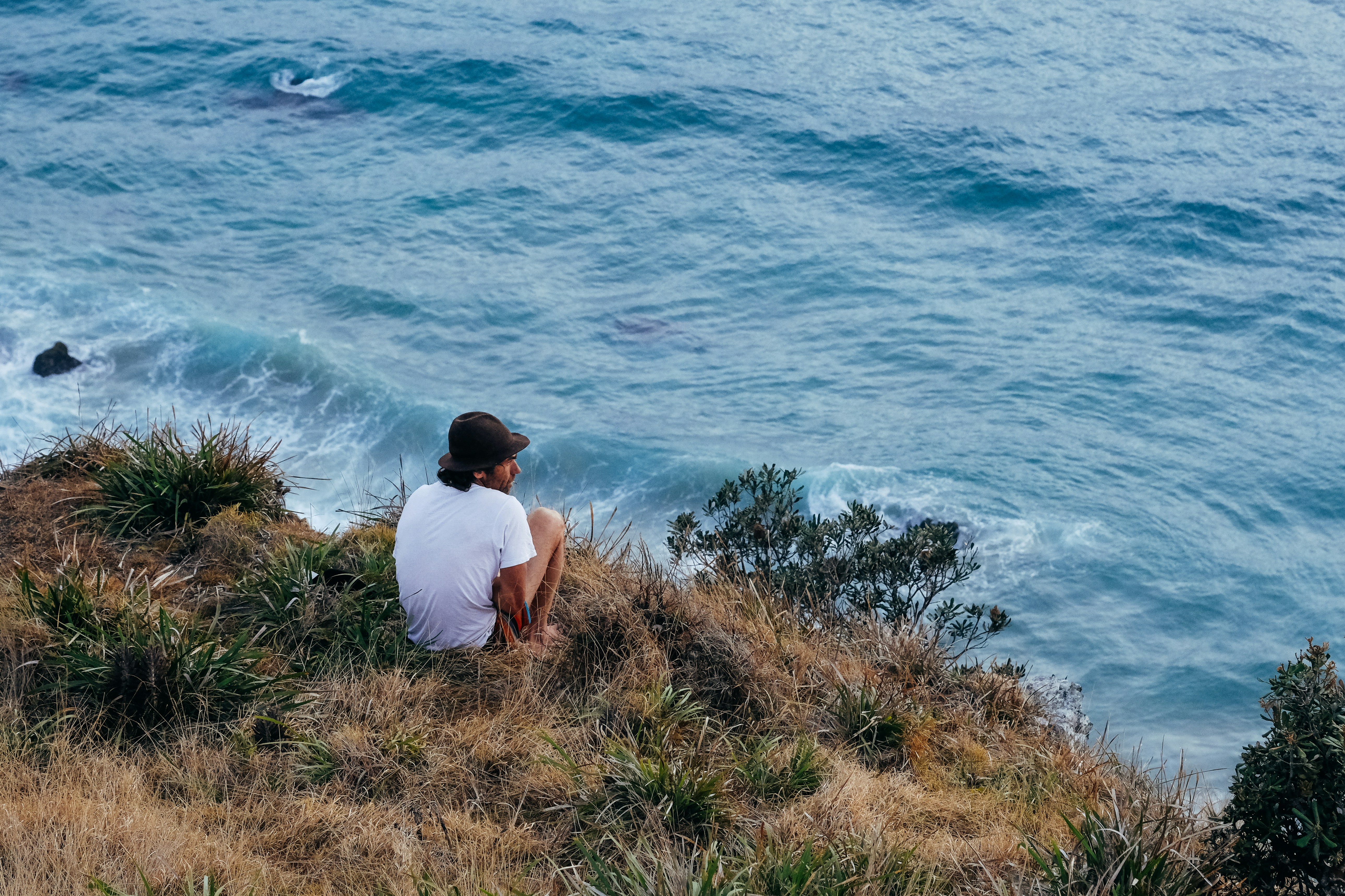 En person som sitter på en klippa med utsikt över ett stormigt hav och ser kontemplativ ut.