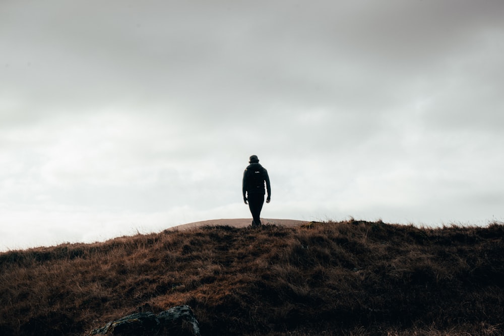 uomo in giacca nera in piedi sul campo di erba marrone sotto il cielo nuvoloso bianco durante il giorno