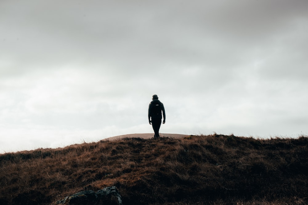 man in black jacket standing on brown grass field under white cloudy sky during daytime