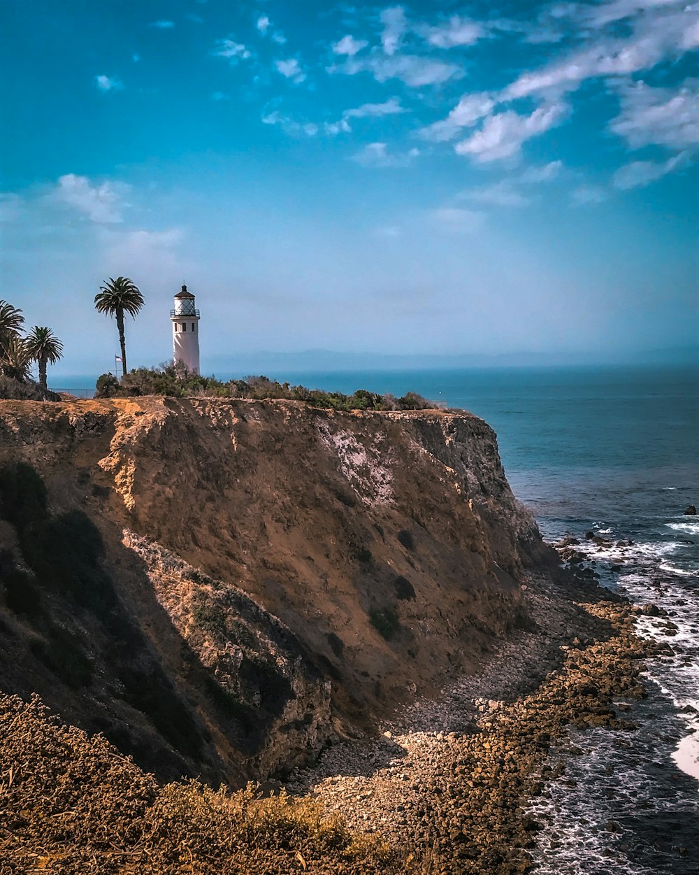 white lighthouse on brown rock formation near body of water during daytime