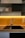 A modern kitchen features clean lines with open shelving filled with neatly stacked white dishes. The focal point is the sleek, metal faucet centered above a dark, square sink set into a wooden countertop. A warm, yellow backlighting adds a cozy, inviting glow to the minimalist design.
