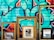 Three ornate picture frames are positioned against a vibrant graffitied wall. Within the frames, there is a painting depicting an outdoor scene, a black and white photograph of a person, and a reflective mirror. The graffiti features abstract shapes and bold colors.