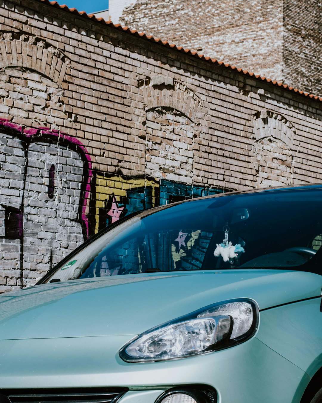 blue car parked beside brown brick wall