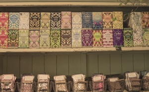 A selection of Pukka tea boxes arranged neatly on wooden shelves. Each box features vibrant and diverse artwork, showcasing various flavors such as peppermint, night time, and elderberry. Below the tea boxes, wire baskets hold additional packaged products.