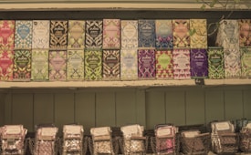 A selection of Pukka tea boxes arranged neatly on wooden shelves. Each box features vibrant and diverse artwork, showcasing various flavors such as peppermint, night time, and elderberry. Below the tea boxes, wire baskets hold additional packaged products.