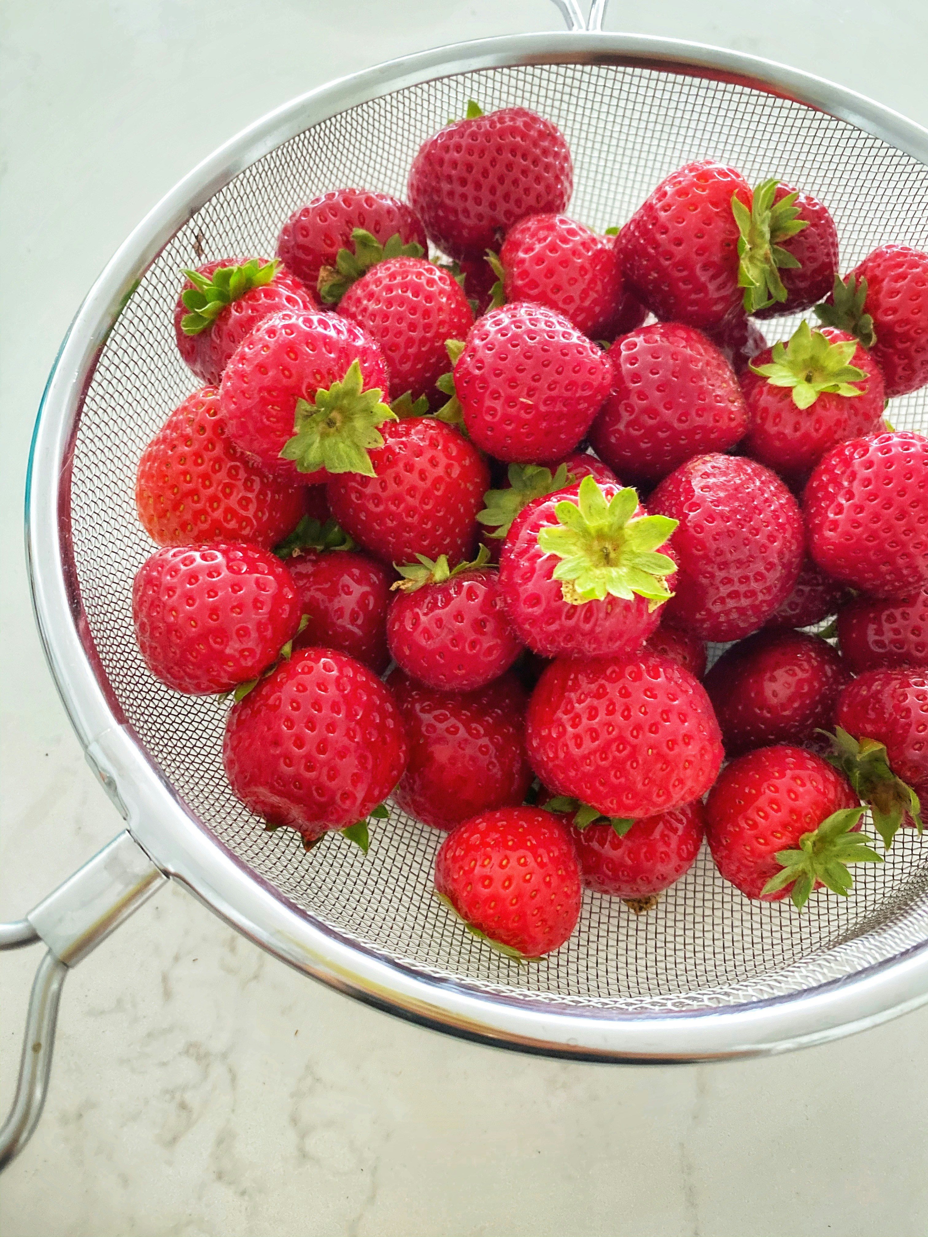 Red strawberries in a colander on a marble kitchen counter.