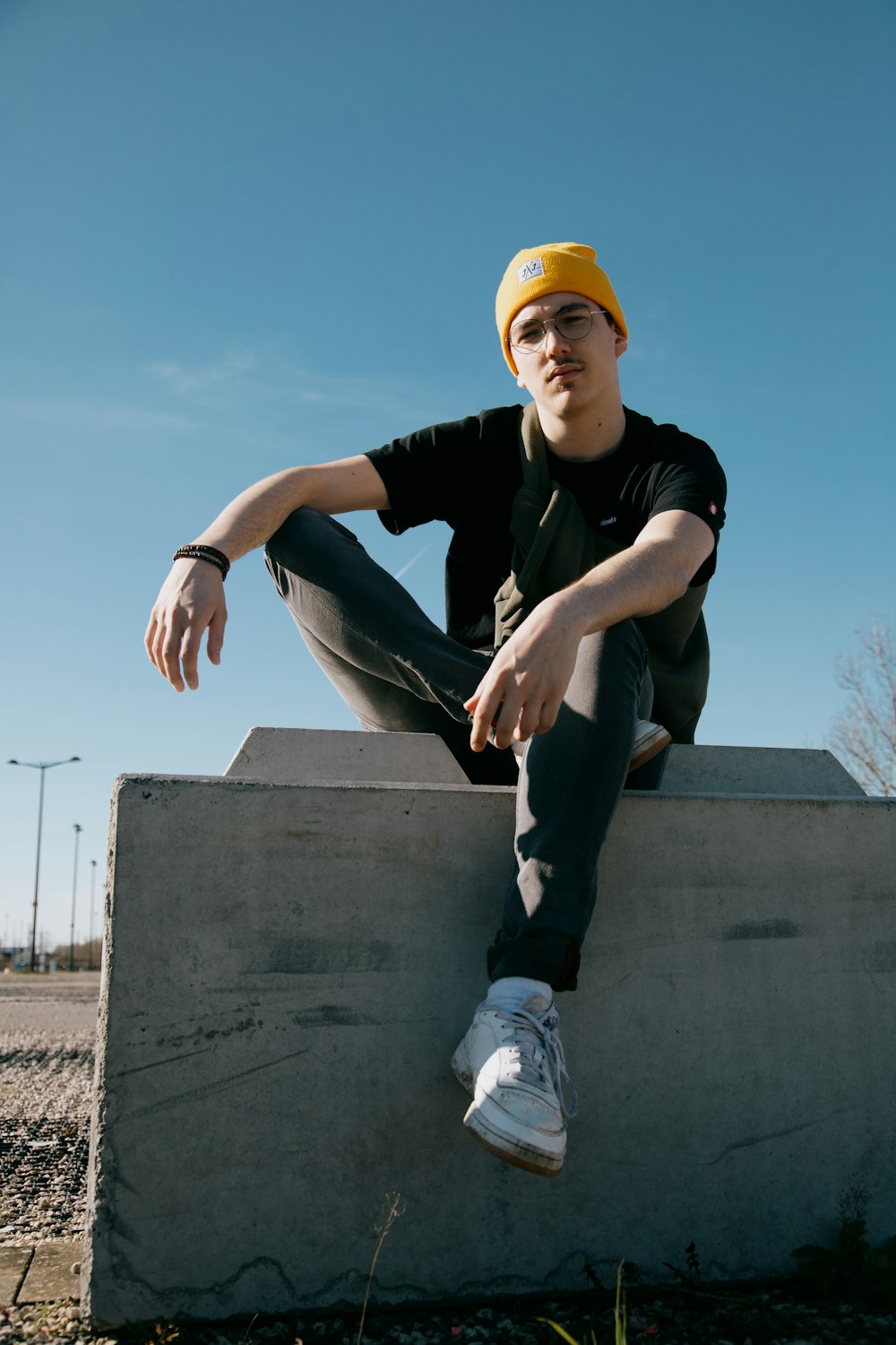 man in black t-shirt and yellow cap sitting on concrete wall during daytime