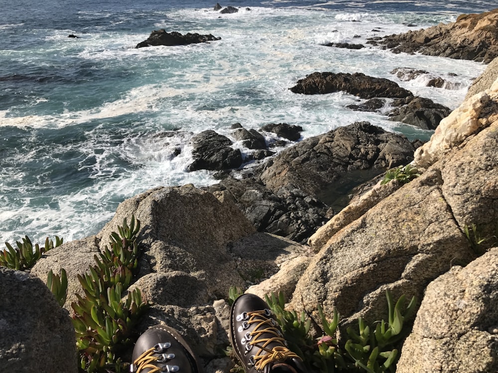 person wearing brown leather shoes on rocky shore