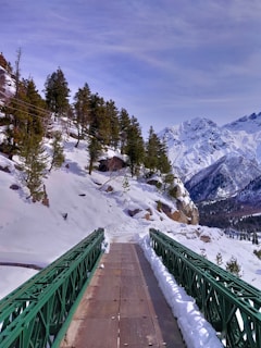 green metal bridge over snow covered mountain during daytime
