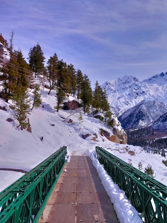 green metal bridge over snow covered mountain during daytime in Chitkul India
