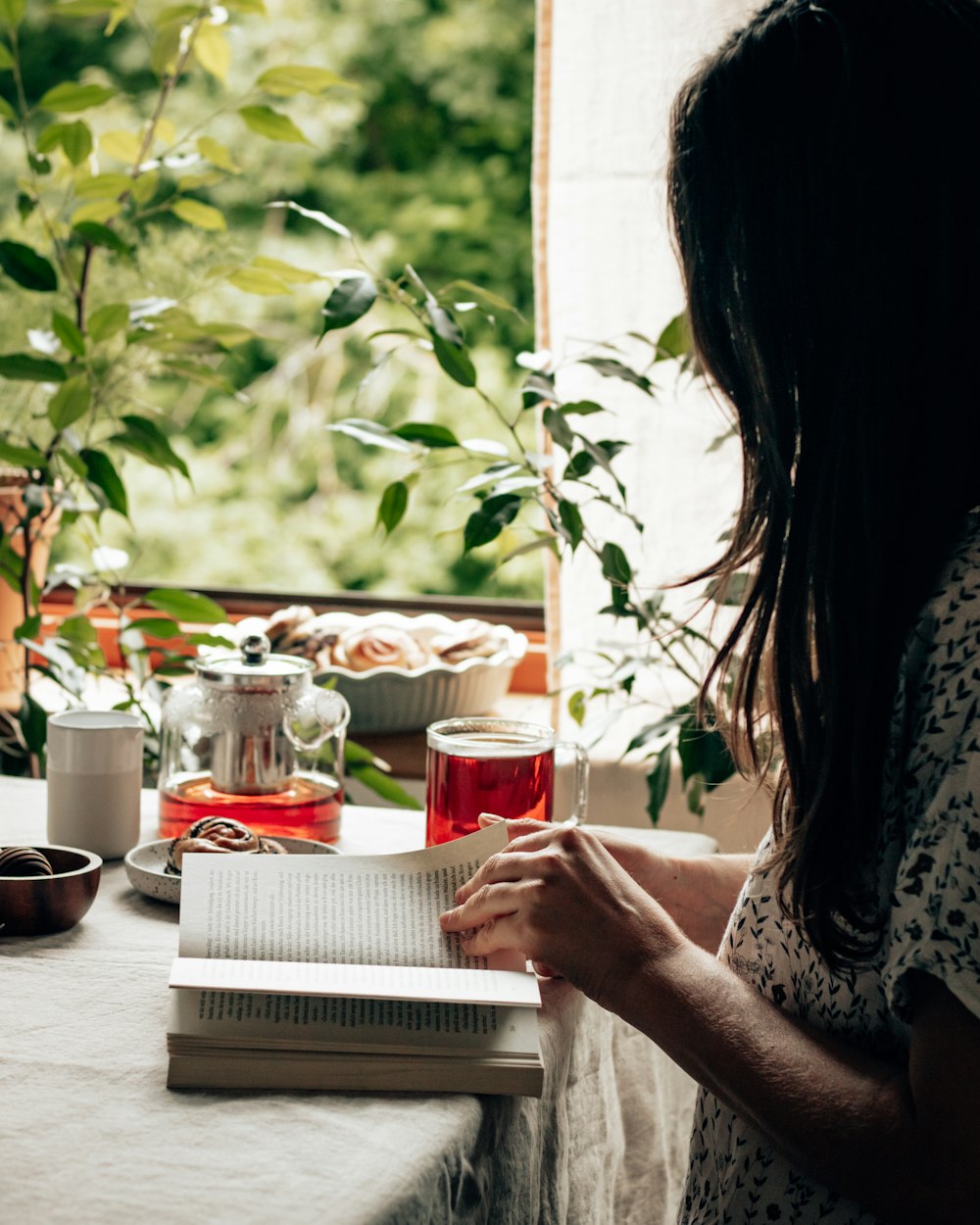 woman in white and black floral dress holding red ceramic mug