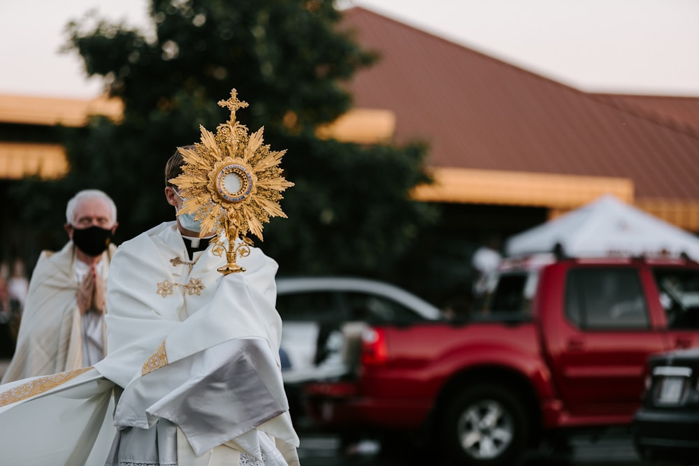 man in white dress shirt wearing gold crown standing near red suv during daytime