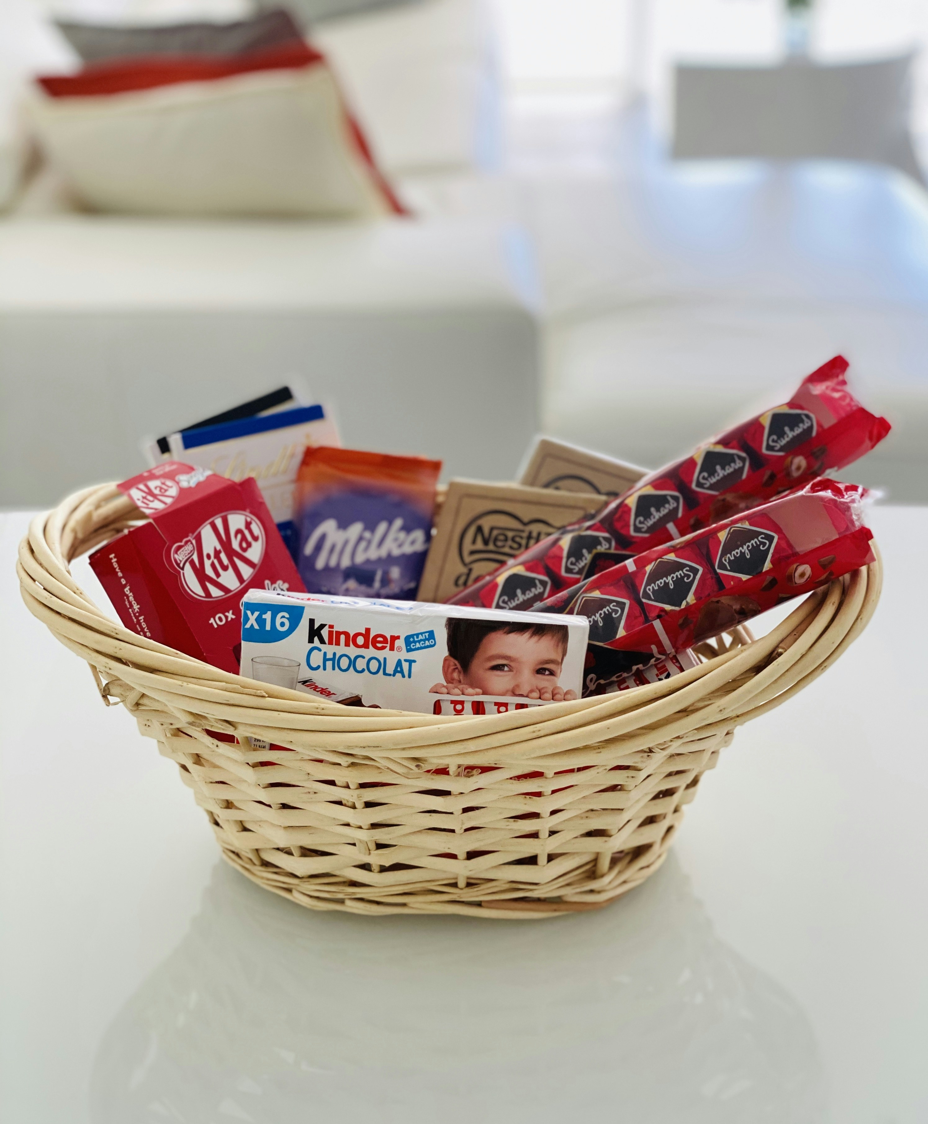 Wicker gift basket filled with gourmet chocolates, cookies, and festive treats wrapped in red cellophane