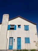 Front view of the white Vendée family house with distinctive red shutters under a bright sky.