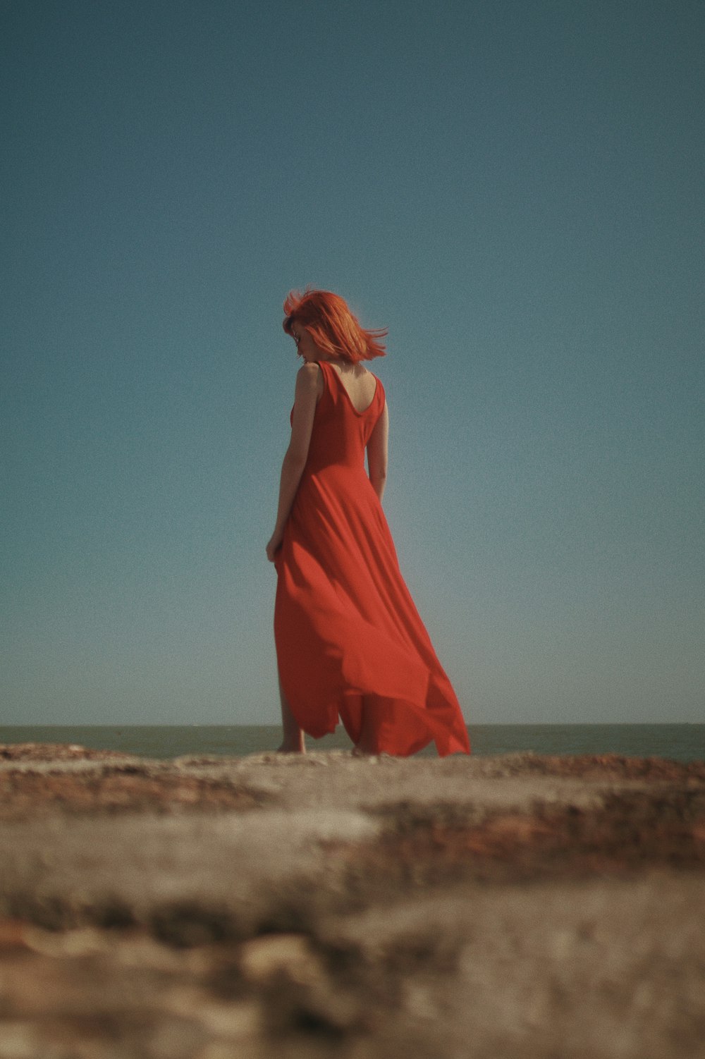 woman in orange dress standing on brown sand during daytime
