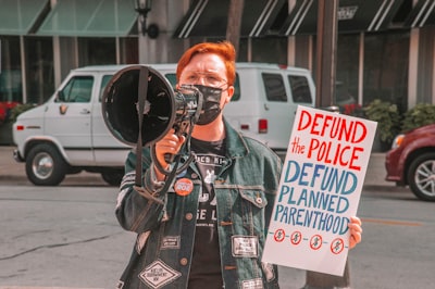 man in black leather jacket holding black dslr camera democrat google meet background