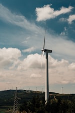 A wind turbine standing tall against a backdrop of rolling green hills.