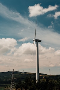 A wind turbine standing tall against a backdrop of rolling green hills.