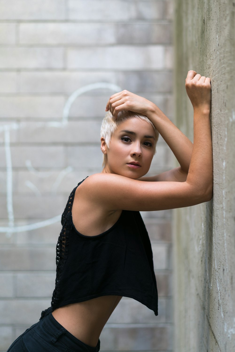 woman in black tank top leaning on gray concrete wall