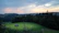 Sunset view over a peaceful forest clearing with a rustic cabin in the distance.