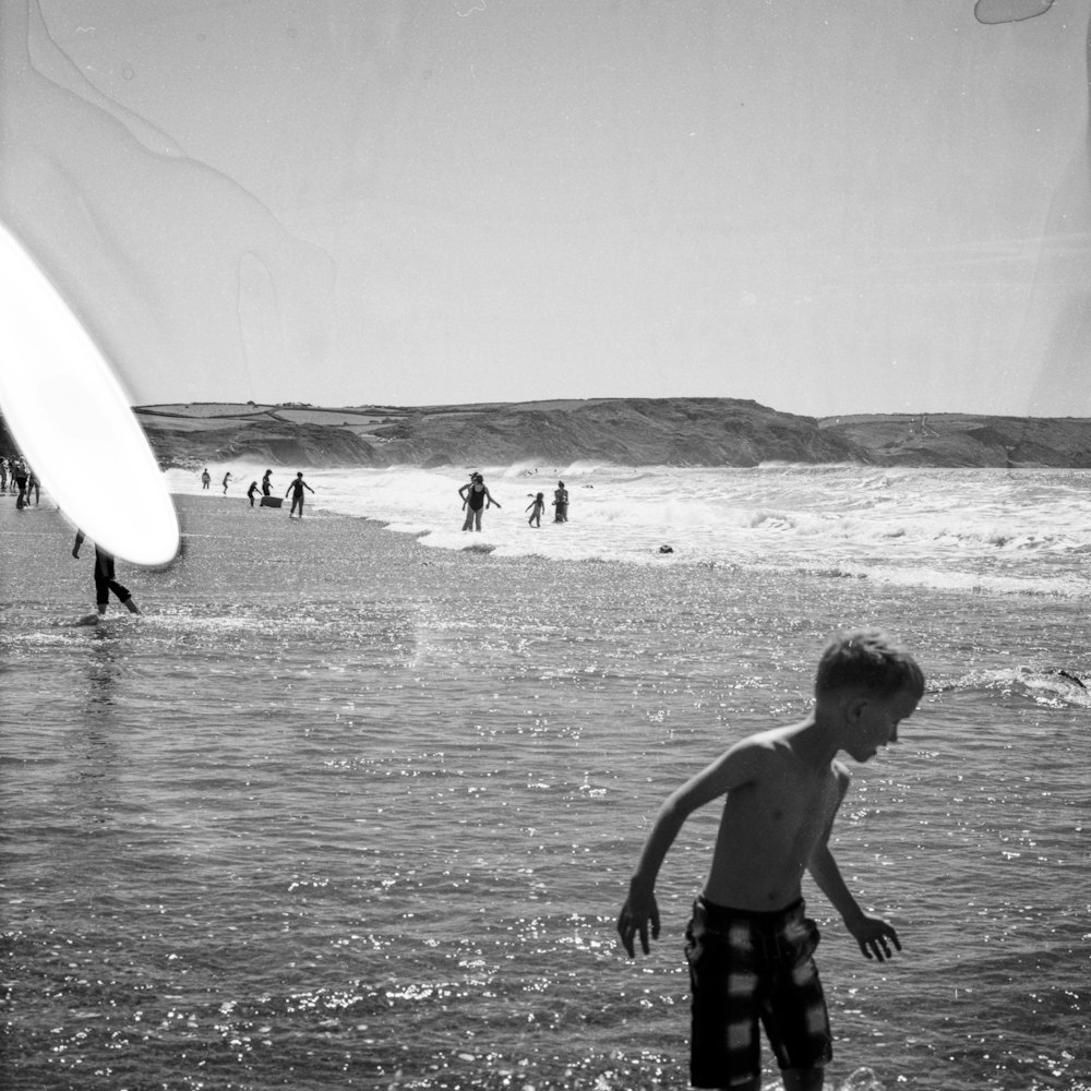 Foto in scala di grigi di un ragazzo che tiene una tavola da surf sulla spiaggia