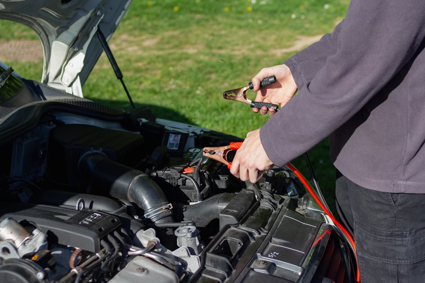 person in grey shirt jump starting a car battery with red and black jumper cables