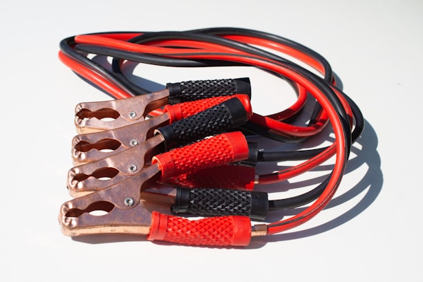 A set of jumper cables with copper clips and insulated handles. The cables are red and black, coiled together with prominent textured grips.