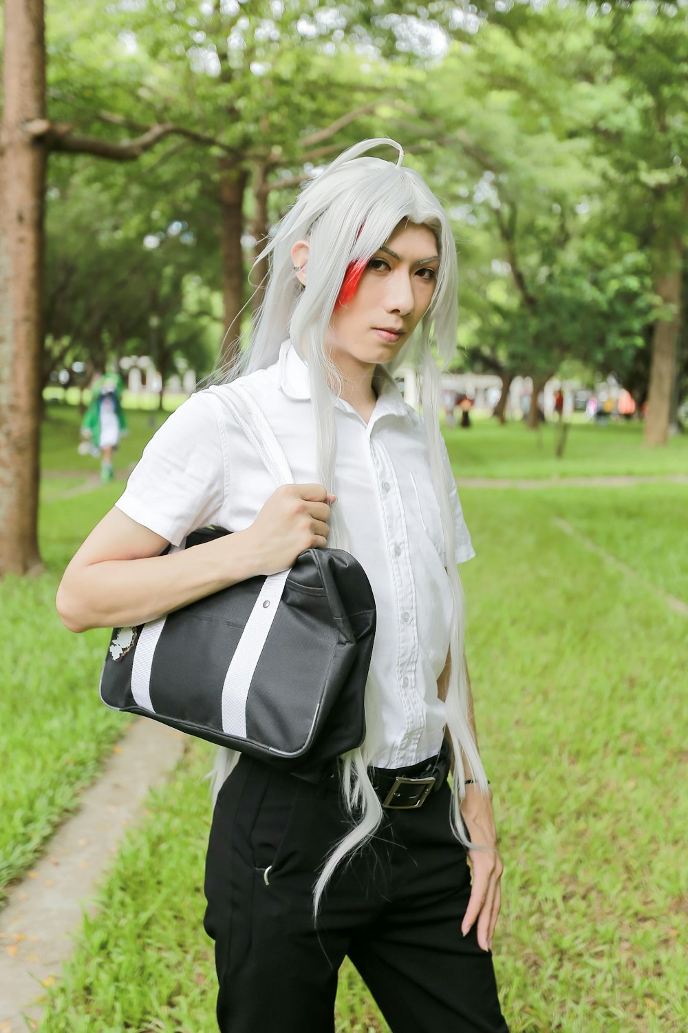 woman in white button up shirt and black and white backpack standing on green grass field