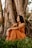 woman in orange tube dress leaning on brown tree