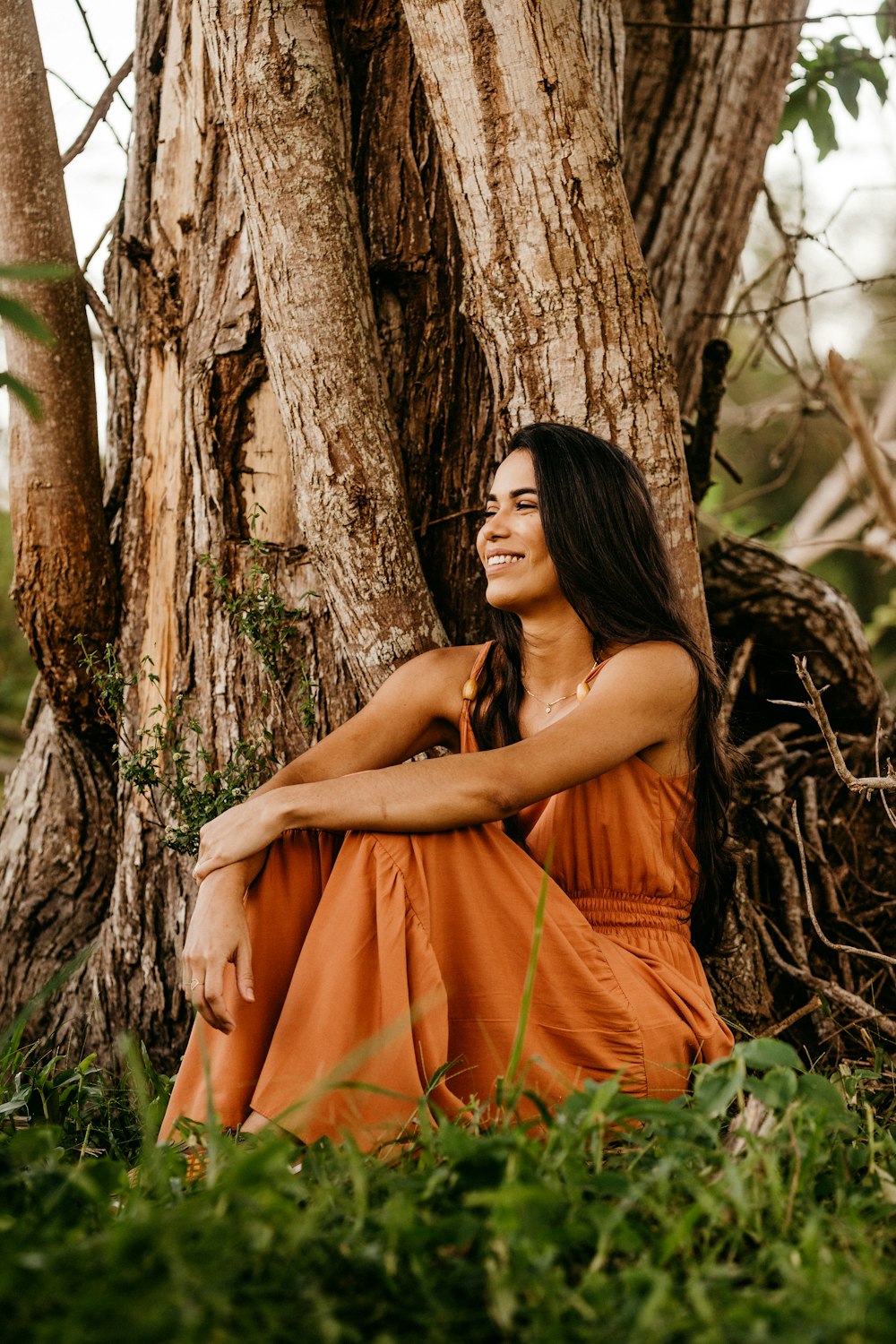 woman in orange tube dress leaning on brown tree