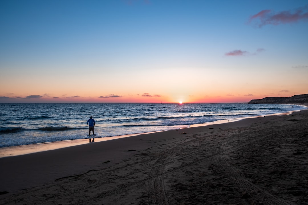 man in black shirt walking on beach during sunset