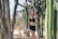 A woman with tattoos is performing a yoga pose, standing on one leg with her arms raised above her head. She is surrounded by tall cacti in a desert-like setting. The woman is wearing a black sports bra and shorts.