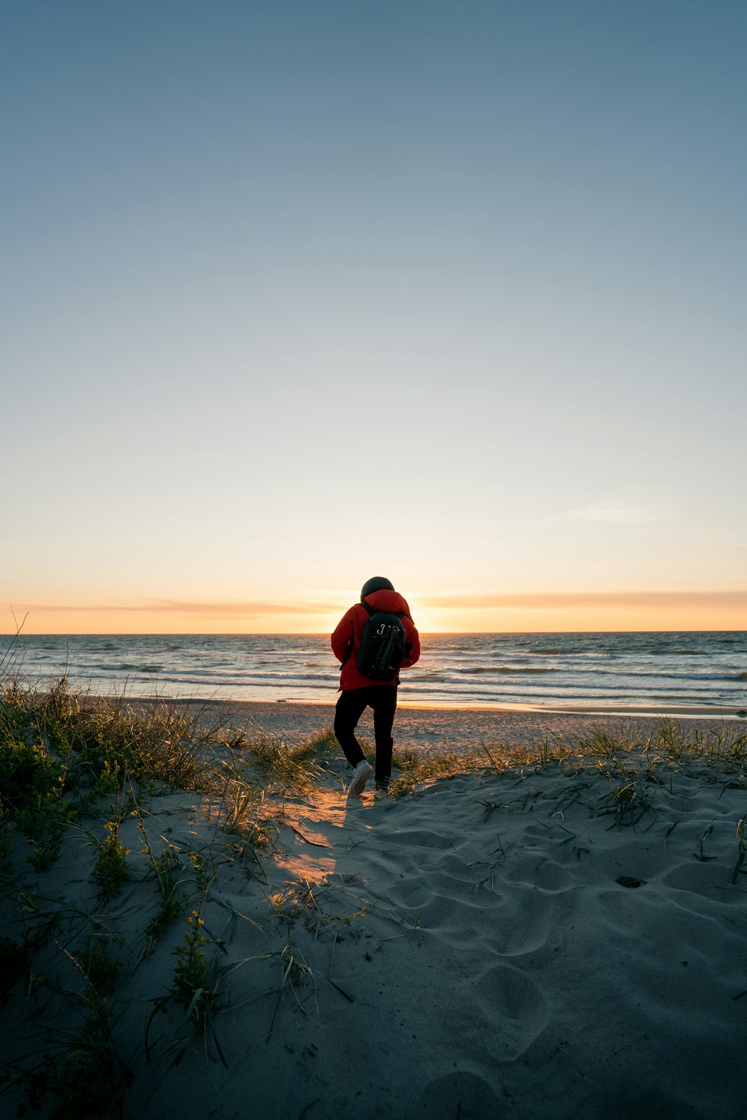 man in red jacket and black pants walking on seashore during daytime