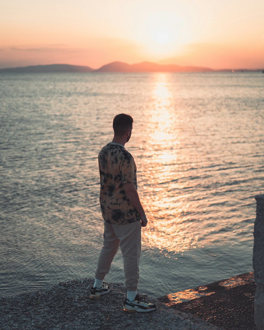 man in brown and black camouflage jacket standing on sea shore during sunset