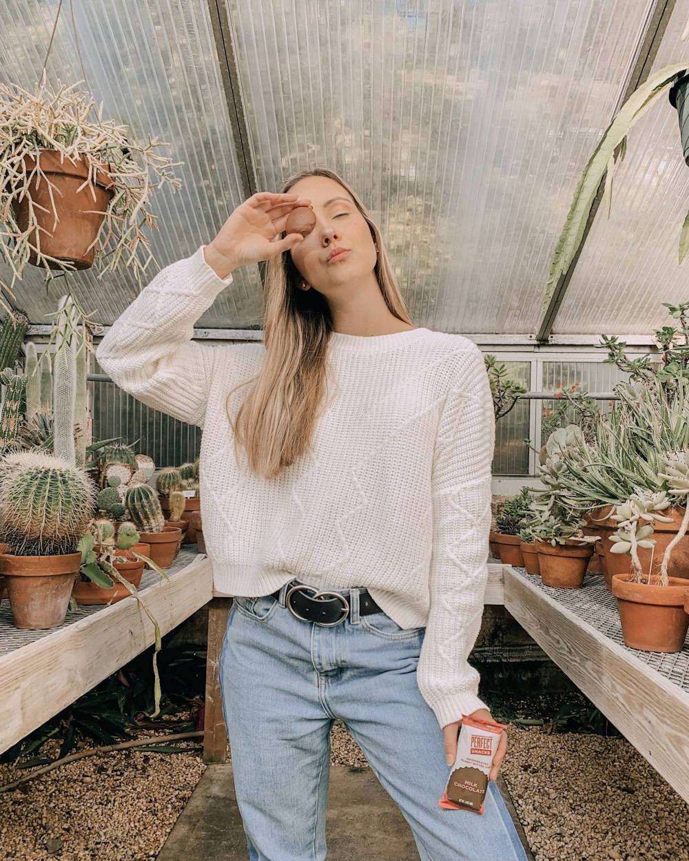 woman in white sweater and blue denim jeans standing near plants