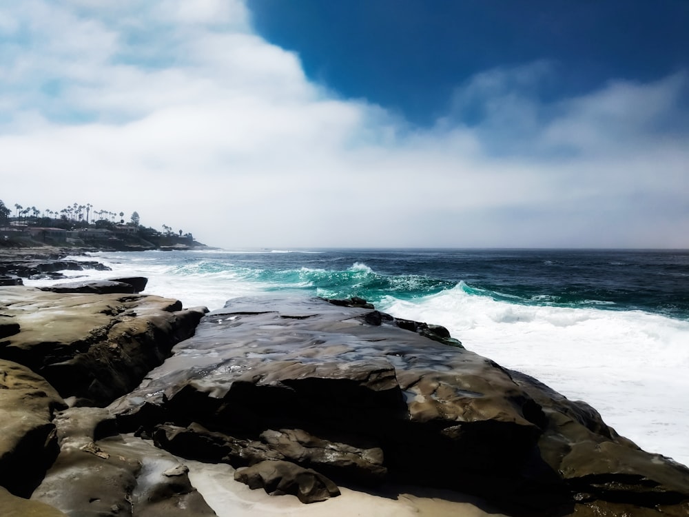 formação rochosa negra perto do mar sob o céu azul durante o dia