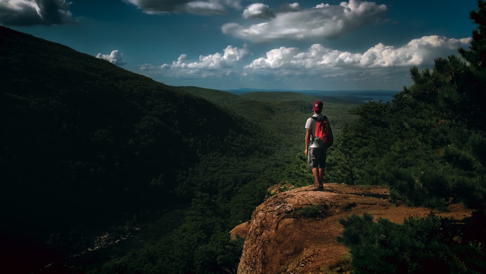 man in black jacket standing on brown rock under blue and white cloudy sky during daytime