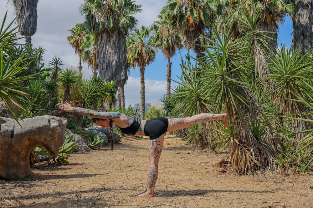 Donna in canotta nera e leggings neri che fa yoga su tronco di legno marrone vicino a verde