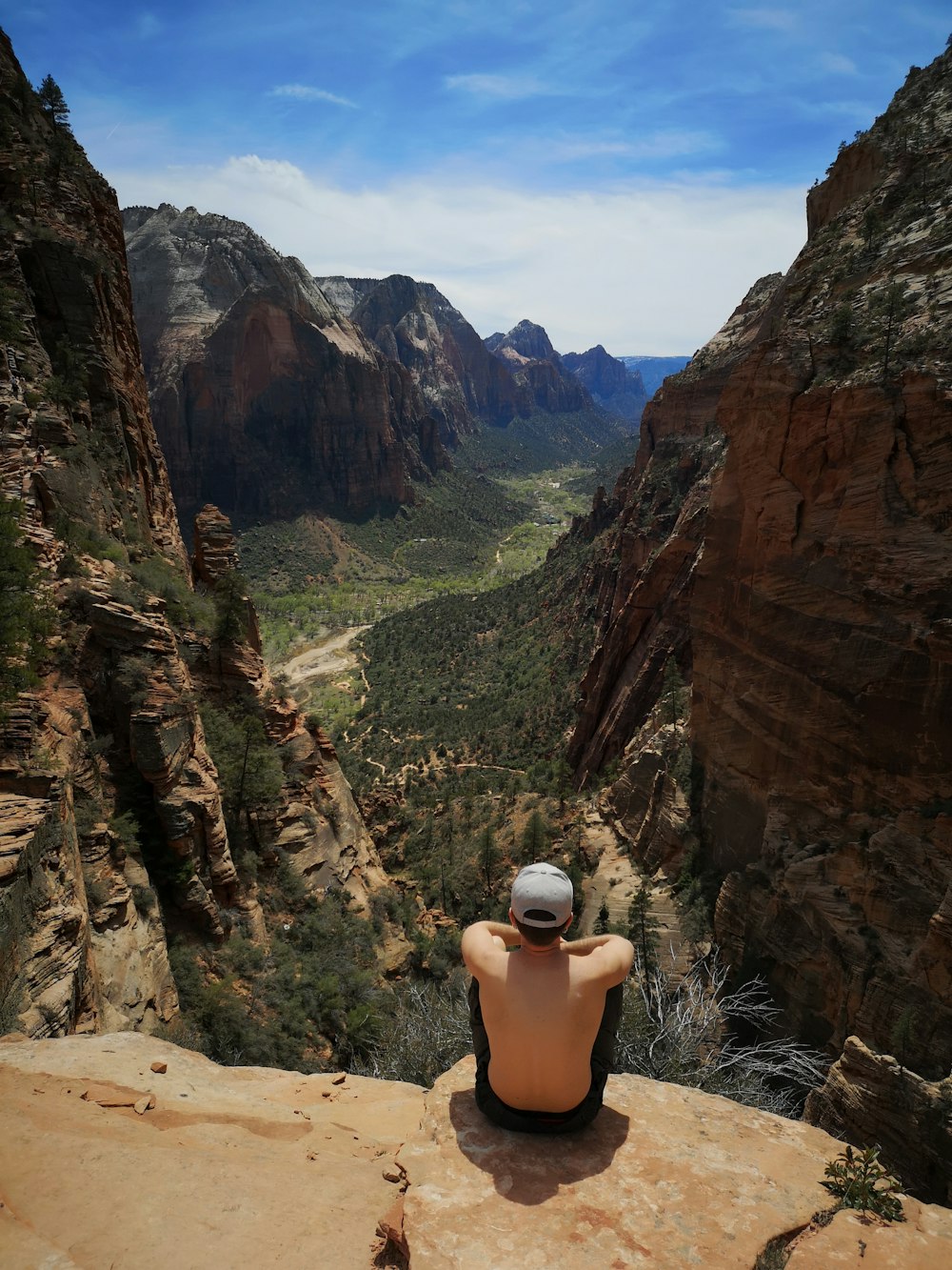 woman in black tank top and white cap sitting on rock formation during daytime