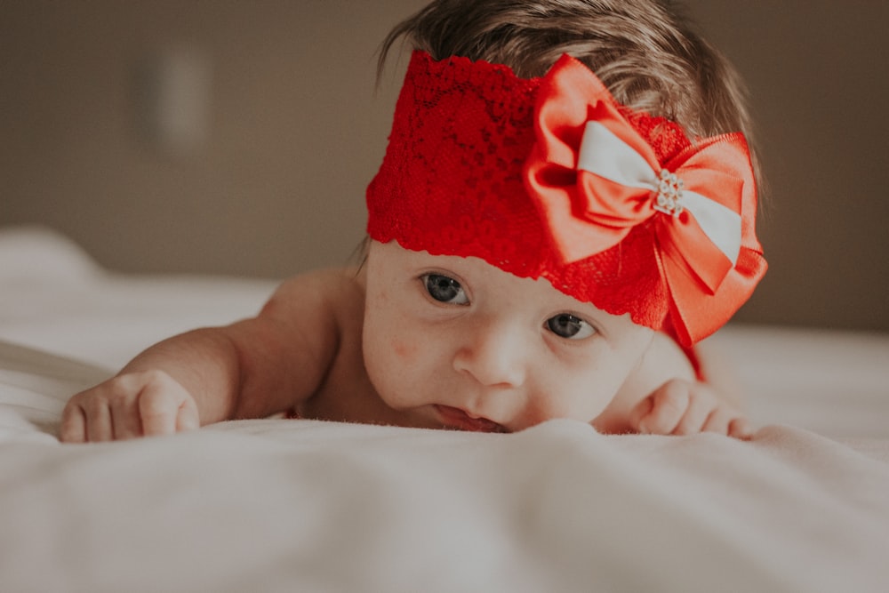 Baby mit roter Blume auf dem Kopf auf weißem Textil liegend