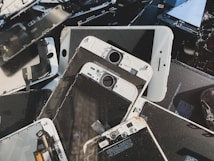 A collection of disassembled and broken smartphone screens and components, primarily displaying the front side of various devices. The parts are scattered in a disorderly manner, displaying signs of wear and damage, including cracked screens and exposed internal circuitry.