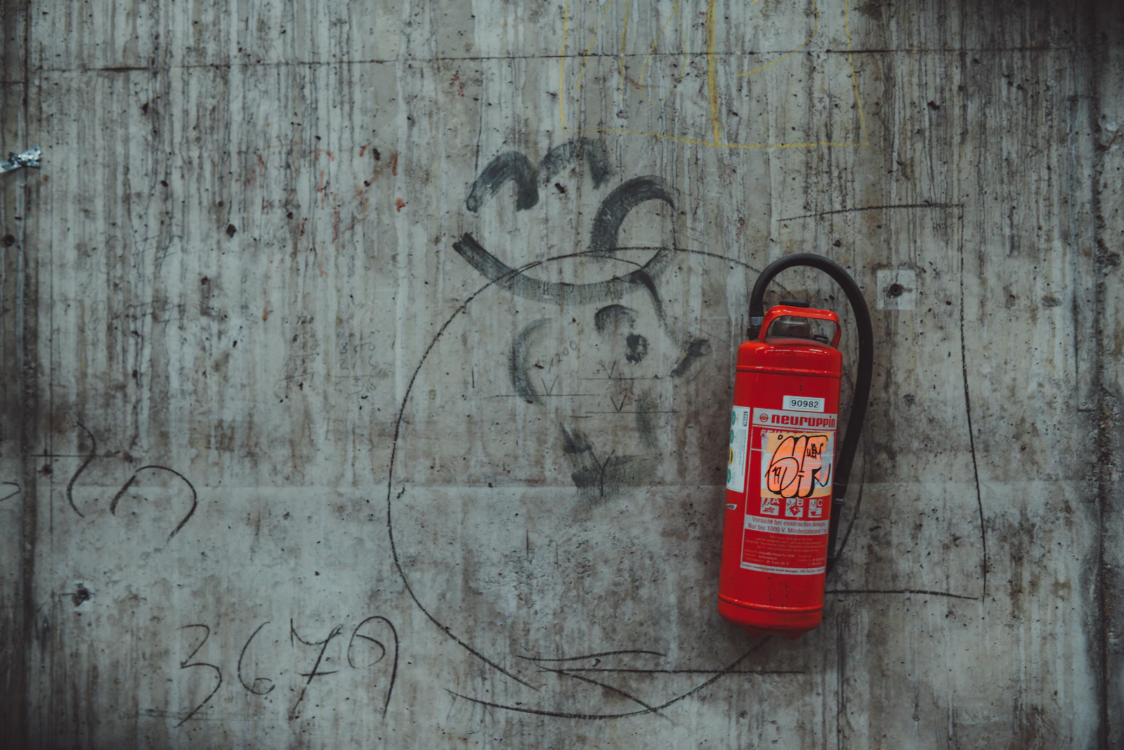 Red fire extinguisher mounted against a weathered concrete wall